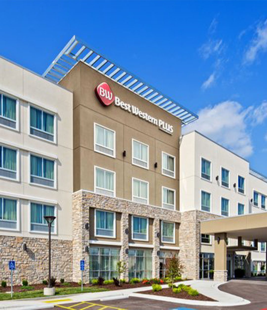 Contemporary Best Western Plus hotel exterior with a mix of tan stone and stucco, several windows, and a clear blue sky in the background.