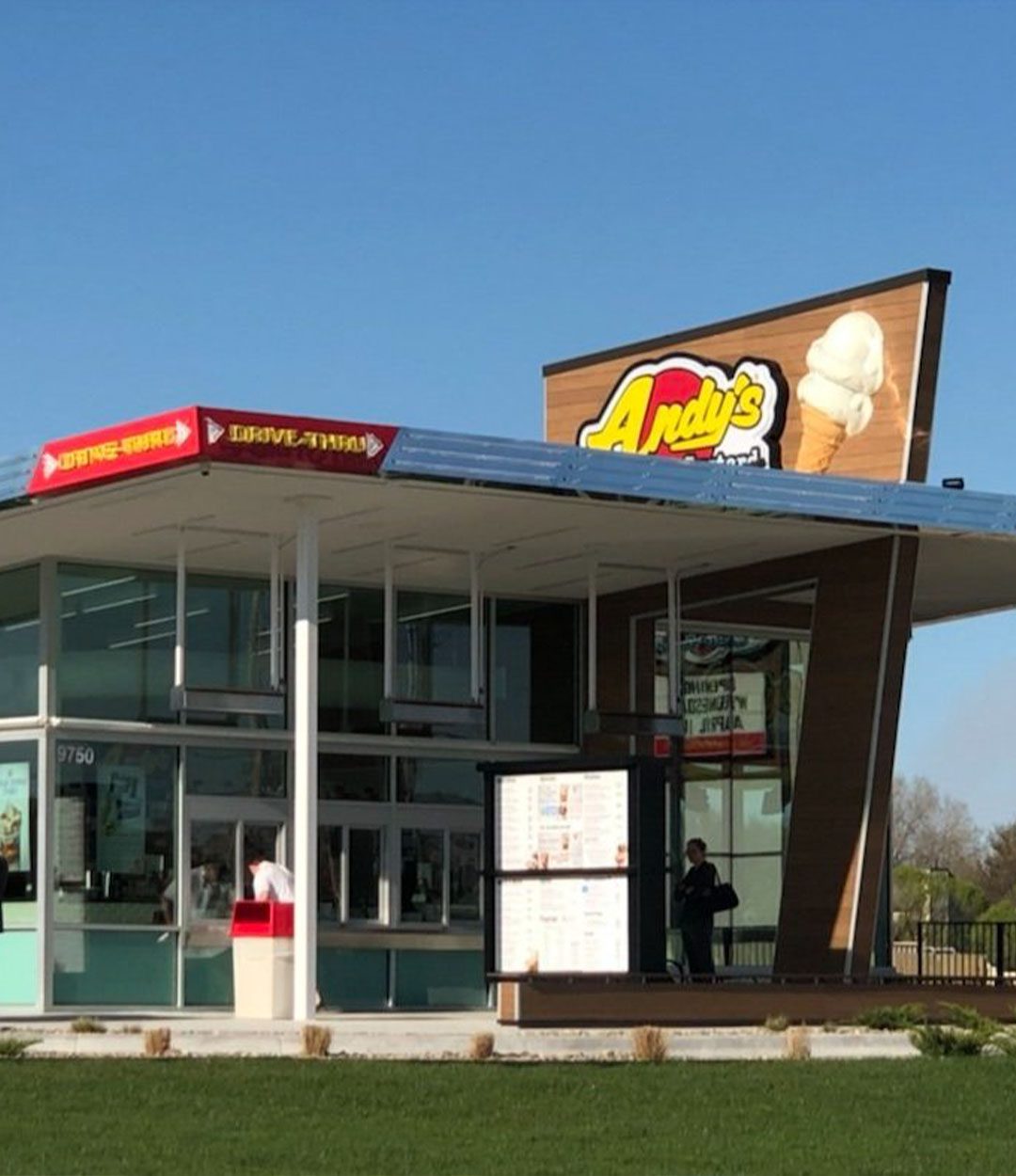 Andy’s Frozen Custard drive-thru and walk-up location with glass walls, angled roof, and large sign displaying an ice cream cone logo.